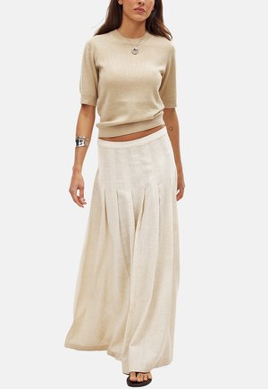 Maglietta beige a maniche corte in maglia con orlo a coste, abbinata a una gonna fluida e plissettata color crema. Il materiale presenta una trama sottile.
