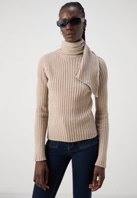 Pull en maille côtelée beige avec un détail de foulard drapé. Fabriqué en matériau doux, avec des manches longues et une silhouette ajustée.