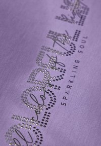 Lila tyg med en glänsande, rhinestone-dekor som stavar "hjärtats färg", med "GLITTRANDE SJÄL" tryckt nedanför.