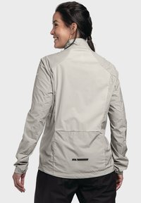 Helle graue Jacke mit hohem Kragen, elastischen Bündchen und einem belüfteten Rücken. Sie hat minimalistische schwarze Akzente und ein elegantes, wasserabweisendes Design.