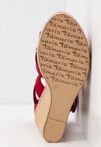 Semelle d’une sandale à talon compensé rouge avec motif logo "tamaris", talon en jute tressée et pointure 37 sur fond clair.