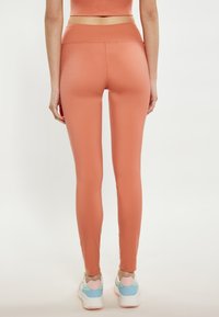 Pfirsichfarbene Leggings mit einer glatten, dehnbaren Textur und einem hohen Bund. Getragen mit bunten Sportschuhen.