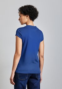 Modré bavlněné tričko s krátkým rukávem, kulatým výstřihem a hladkou texturou, spárované s tmavě modrými džíny s prošíváním na zadních kapsách.