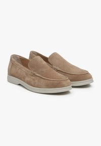 Beżowe zamszowe buty slip-on z okrągłym noskiem, ozdobnym przeszyciem oraz kontrastującą białą gumową podeszwą. Miękka tekstura i casualowy design.