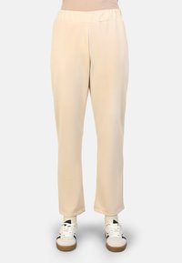 Beige, elastische broeken van gladde stof, met taps toelopende benen en zijzakken, gecombineerd met witte sneakers.