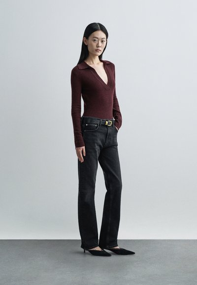 Bordový body s dlhými rukávmi a hlbokým výstrihom do V, v kombinácii s čiernymi džínsami s rovnými nohavicami a čiernymi lodičkami s ostrou špičkou, s čiernym opaskom.