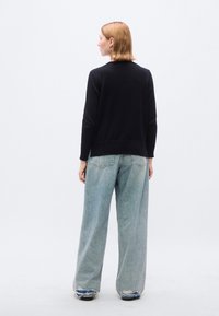 Maglione nero lavorato a maglia con scollo rotondo, abbinato a jeans a vita alta, a gamba larga e di colore azzurro chiaro, caratterizzati da orlo sfilacciato e tasche.