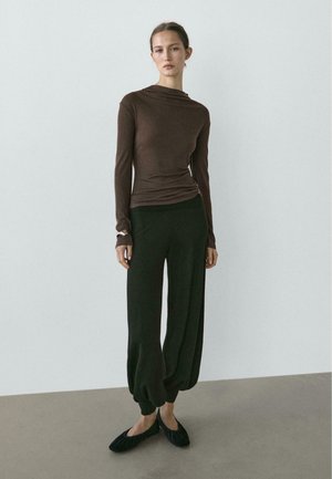 Haut marron à manches longues avec un col drapé, associé à un pantalon ample vert foncé et des chaussures plates noires. Tissu simple et doux avec une coupe décontractée.
