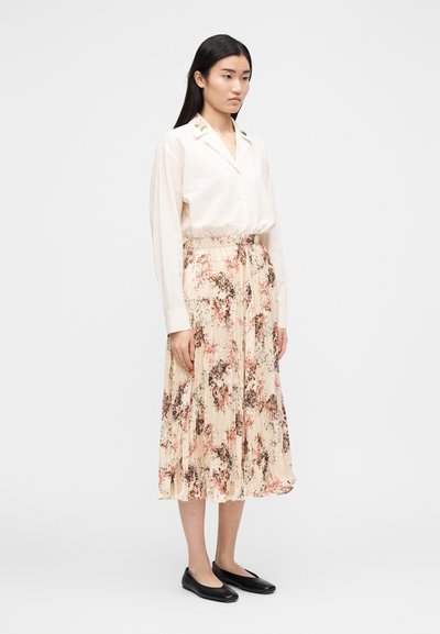 Cream blouse with floral embroidery on the collar, paired with a pleated, ankle-length floral skirt in soft pink and beige tones, complemented by black flats.