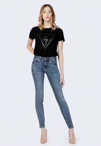 T-shirt nera a maniche corte con un design grafico triangolare, abbinata a jeans aderenti azzurri e scarpe con tacco nude.