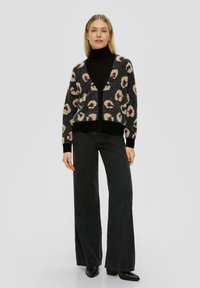 Zwart en beige panterprint cardigan met een V-hals, knoopsluiting en geribbelde manchetten, gecombineerd met hoge taille zwarte jeans en zwarte laarzen.