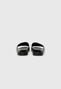 Sandales noires au design minimaliste, dotées d'une semelle plate, d'un bout ouvert et de lanières courbées pour une silhouette élégante.