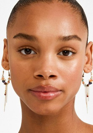 Kullatooni kõrvarõngad mitme kujuga värviliste helmestega, millel on rippuvad kettid, mis lisavad liikumist ja visuaalset huvi.