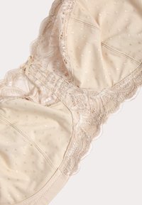 Beige kanten beha met doorschijnende polkadot mesh cups, gegolfde kanten randen en een klein decoratief strikje in het midden aan de voorkant.