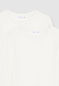 Due t-shirt bianchi a maniche lunghe impilati, realizzati in morbido cotone, con scollatura rotonda e etichetta del marchio con indicazione della taglia 'S'.