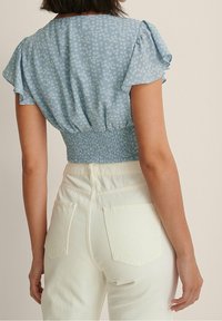 Haut bleu à motif floral avec manches courtes à volants et taille smockée, associé à un jean ajusté taille haute de couleur claire.