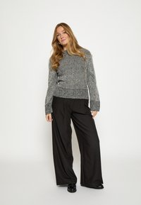 Szary sweter w paski z dzianiny z długimi rękawami i ściągaczami przy mankietach, połączony z czarnymi szerokimi spodniami i czarnymi butami. Prosty, nowoczesny design.