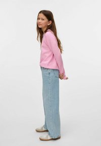 Różowa bluzka z długim rękawem połączona z jasnoniebieskimi spodniami o szerokich nogawkach i beżowymi trampkami. Materiał jest miękki, z luźnym krojem i prostym wzorem.