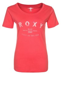 Korálové tričko s krátkým rukávem vyrobené z bavlny, s kulatým výstřihem a textem "ROXY EST 1989 WEST OF THE ONE" v bílých grafikách.