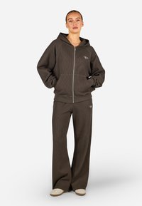 Brązowa, prążkowana bluza z zamkiem błyskawicznym, z dużymi kieszeniami i luźnym krojem, połączona z pasującymi szerokimi spodniami. Dyskretne logo na obu elementach.
