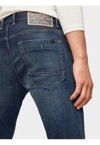 Jeans de mezclilla azul oscuro con un ajuste slim, que cuentan con una etiqueta de cuero en la cintura y un bolsillo trasero con sutiles detalles de costura.