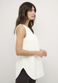Blusa bianca senza maniche con scollatura rotonda, orlo curvo e dettaglio a bottoni sulla parte frontale. Tessuto morbido con una superficie liscia.