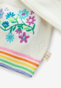 Maglione bianco lavorato a maglia con ricami floreali colorati in blu, viola e verde, dotato di un orlo a coste multicolore e un'etichetta.