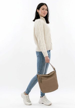 Pull beige en maille torsadée, jean skinny bleu clair et baskets blanches, portant un sac à bandoulière en cuir marron avec un détail en fermeture éclair.