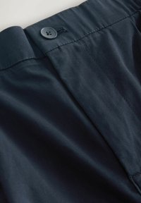 Pas kalhot v námořnické modři s hladkým povrchem, zapínáním na knoflík a prošitím podél okrajů.