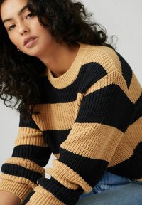 Maglione in maglia grossa con ampie strisce nere e beige, texture a coste e scollatura rotonda. Presenta polsini arrotolati e una vestibilità rilassata.