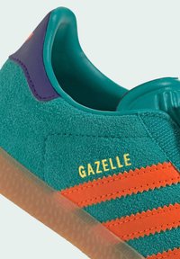 Teal suede sneaker with orange accents and zigzag stripes. Features a purple heel tab and visible lacing, labeled "GAZELLE" in yellow.