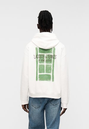 Sudadera blanca con capucha y un diseño gráfico verde de una pista de tenis en la espalda, con texto en negro. Corte holgado, tejido suave y puños acanalados.