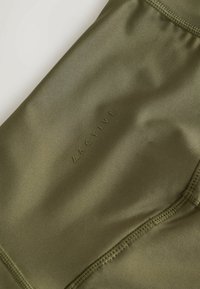 Gros plan sur un tissu extensible vert olive avec des coutures visibles et le texte "ACTIVE" embossé en couleur assortie sur un matériau de vêtements de sport.