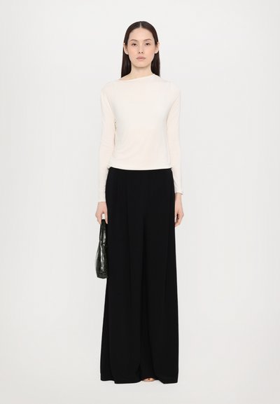 Bluză crem cu mânecă lungă, gât înalt; pantaloni negri evazați, cu față plăcută. Ținând o geantă neagră, cu model de crocodil. Design simplu, elegant.