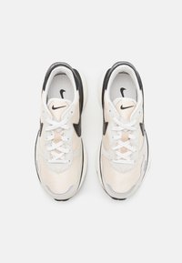 Baskets Nike en beige et noir, avec une tige en maille, des accents en tissu, des lacets blancs et une semelle texturée à la forme arrondie.