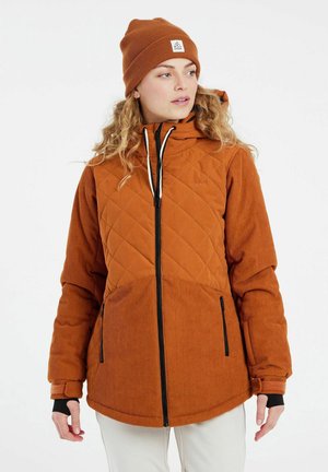 Giacca trapuntata marrone con una texture in velluto a coste e zip nere, abbinata a un berretto a coste coordinato. Presenta un cappuccio e tasche laterali.