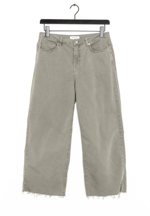 Pantalons larges gris clair avec des ourlets effilochés suspendus à un cintre noir sur fond blanc.