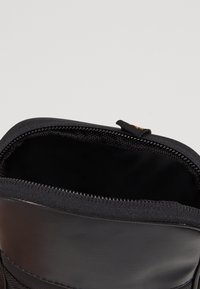 Musta vetoketjullinen laukku, jossa on sileä ulkopinta, vahvistettu yläreuna ja pehmeä musta vuori. Varustettu metallivetoketjulla ja kangastarralla sulkemista varten.