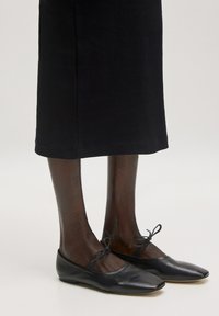 Schwarze Ballettschuhe aus Leder mit einer runden Zehenpartie, akzentuiert durch eine kleine Schleife am Knöchel. Weiche Textur und dünne Sohle.