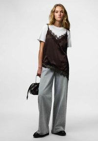 Brun satengcamisole med blonder over en hvit t-skjorte, kombinert med vide, lysegrå jeans og en liten svart veske.