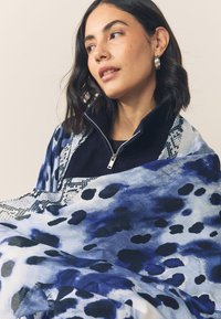 Blue and white patterned scarf with fluid brushstroke design, featuring dark polka dots and a textured finish. Lightweight fabric, soft drape.