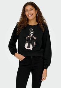 Musthave must, mille mustriga disainiga naine, kellel on lips ja pitsaktsendid, pehmest kangast, mugava lõikega ja pikkade varrukatega.