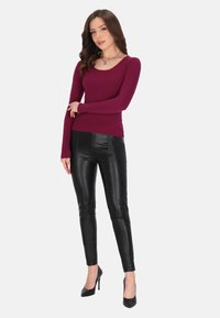 Bordeauxfarbenes geripptes Langarmoberteil, schwarze hochtaillierte Lederhosen und schwarze High Heels. Enganliegende Passform, glatte Textur und runder Ausschnitt.