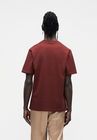 Bordowy bawełniany t-shirt z krótkimi rękawami i okrągłym dekoltem. Prosty, jednolity wzór o miękkiej teksturze i prostym kroju na dole.