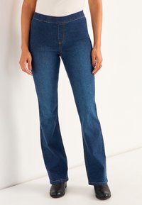 Tumma pesu farkut, joissa on leveä lahje ja korkea vyötärö, näkyvällä ompelulla ja sileällä tekstuurilla. Yhdistetty mustiin jalkineisiin.