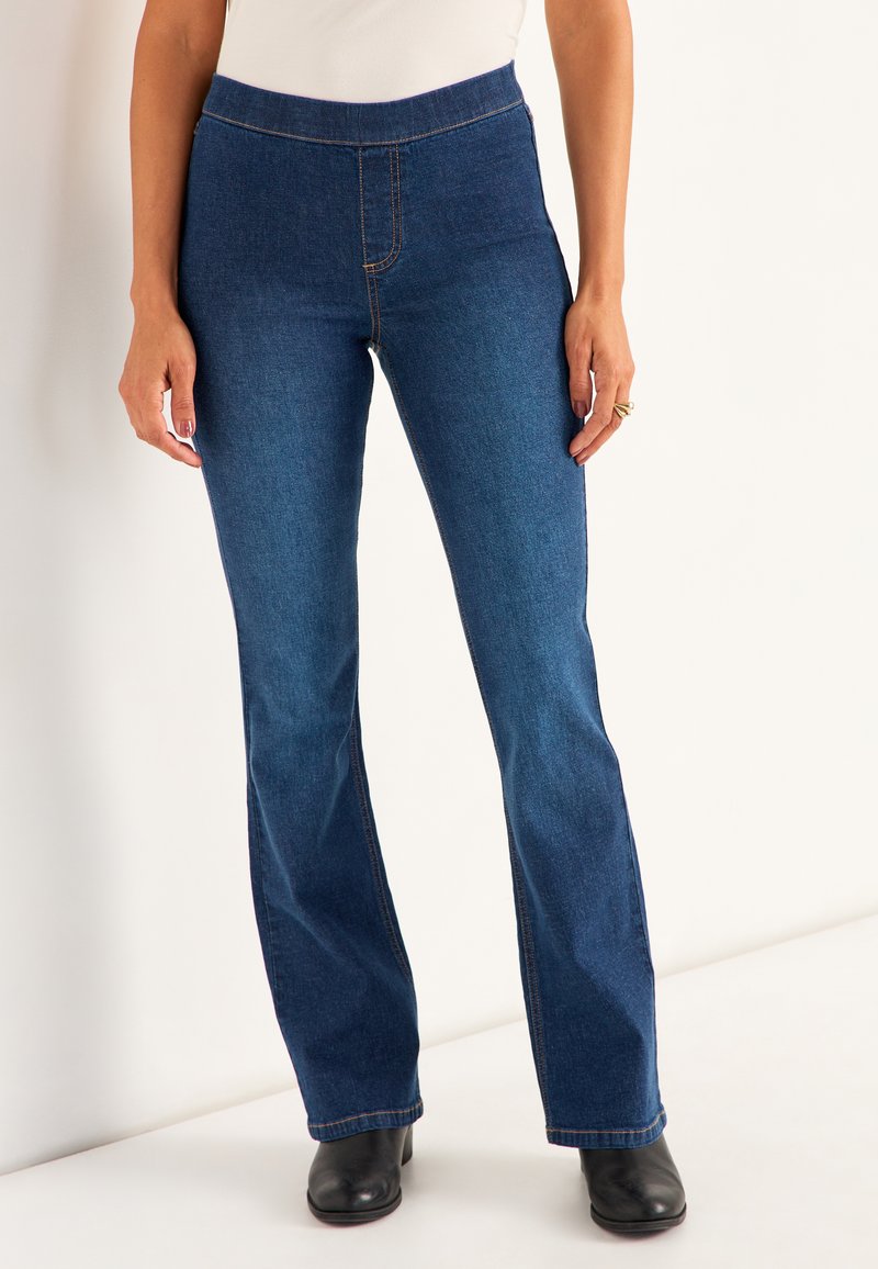 Tumma pesu farkut, joissa on leveä lahje ja korkea vyötärö, näkyvällä ompelulla ja sileällä tekstuurilla. Yhdistetty mustiin jalkineisiin.