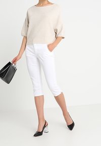 Top de punto beige con mangas cortas y anchas, combinado con pantalones cortos blancos. Bolso negro con herrajes plateados y tacones negros con detalles plateados.