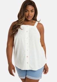 Top in lino bianco senza maniche con scollo quadrato e bottoni lungo la parte anteriore; abbinato a pantaloni corti di denim con risvolto.