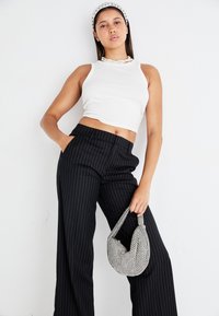 White cropped tank top, black pinstriped wide-leg pants, and a glittery handheld bag. Model poses with one hand in pocket and headband.