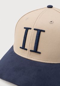 Μπεζ και ναυτικό μπλε καπέλο με κέντημα αριθμό II σε σκούρο μπλε στη μπροστινή πλευρά.